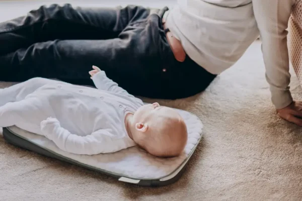 En baby, der ligger på et tæppe ved siden af sin mor.