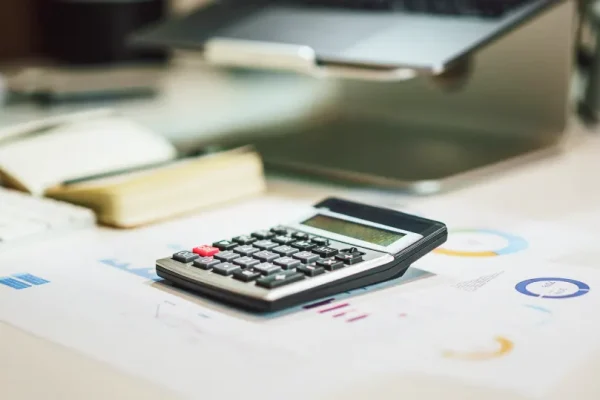 En lommeregner på et bord ved siden af en notesbog og en bærbar.