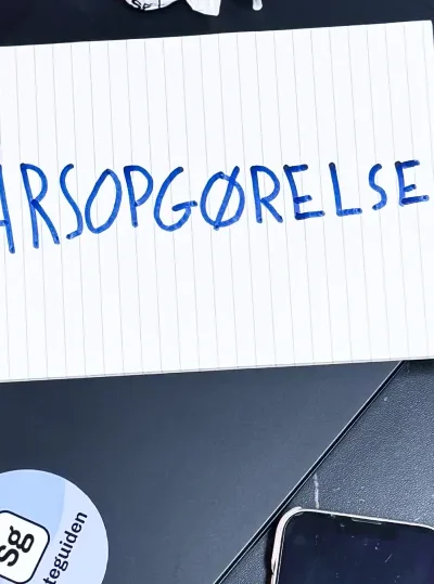 Der står "Årsopgørelse" på et papir, der ligger på et bord ved siden af briller, en bærvar og en telefon.
