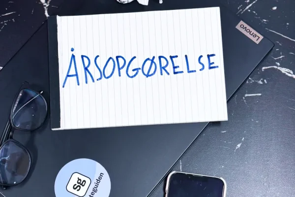 Der står "Årsopgørelse" på et papir, der ligger på et bord ved siden af briller, en bærvar og en telefon.