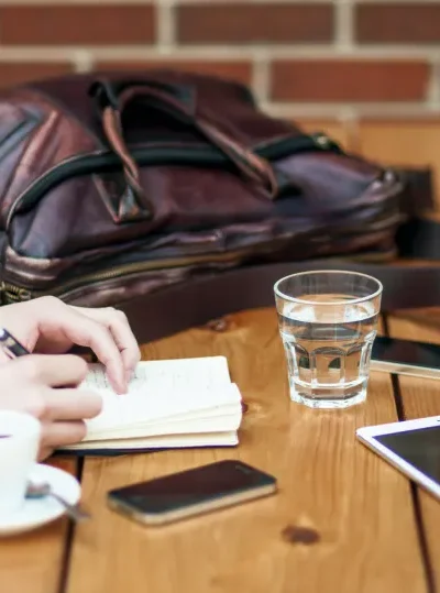 To personer sidder overfor hinanden ved et bord. Den ene skriver i en notesbog og den anden tjekker sine mobile enheder.