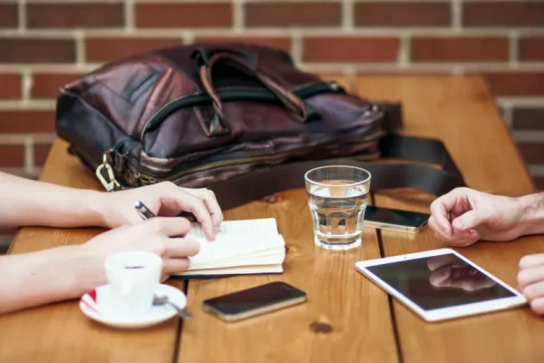 To personer sidder overfor hinanden ved et bord. Den ene skriver i en notesbog og den anden tjekker sine mobile enheder.