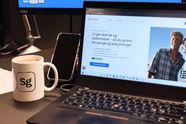 En laptop, der viser forsiden af Skatteguidens hjemmeside ved siden af en mobil og en kaffekop.
