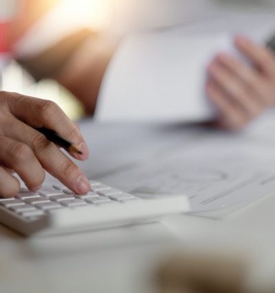 Lommeregner og en person, der taster og laver beregner med en kuglepen i hånden.